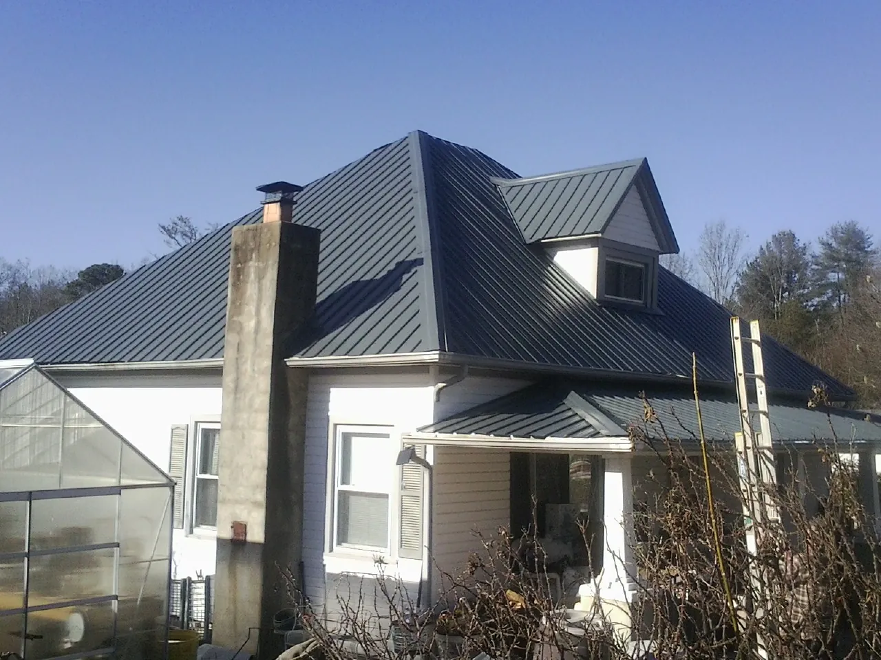 Dark blue standing seam metal roof on a white farmhouse with dormer — Slate & Tile Roof Repair by Roofing Brothers in Vintondale