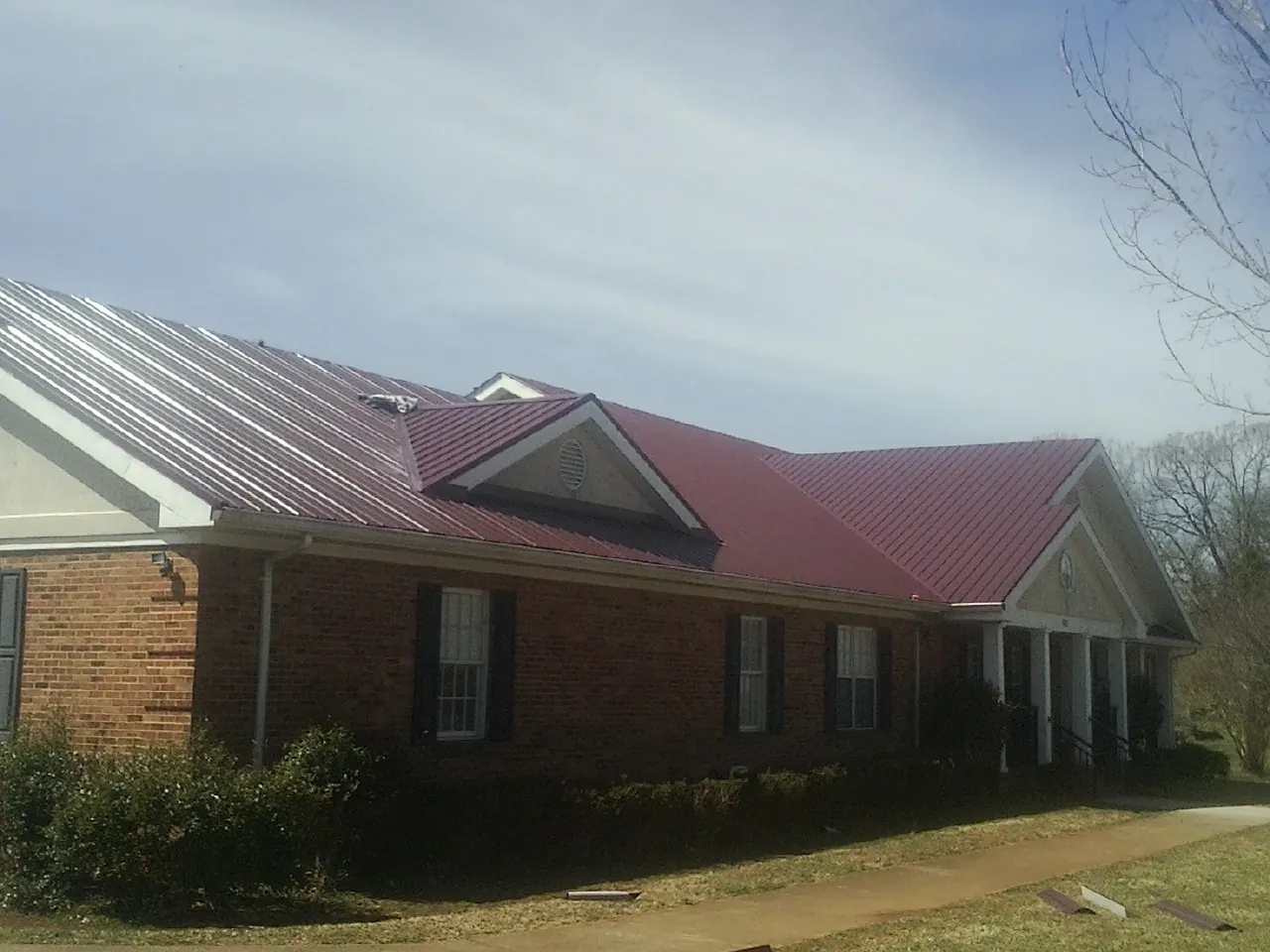 Red metal roof with gabled entries on a long brick building, from a Hail Damage Roof Repair job in Vintondale