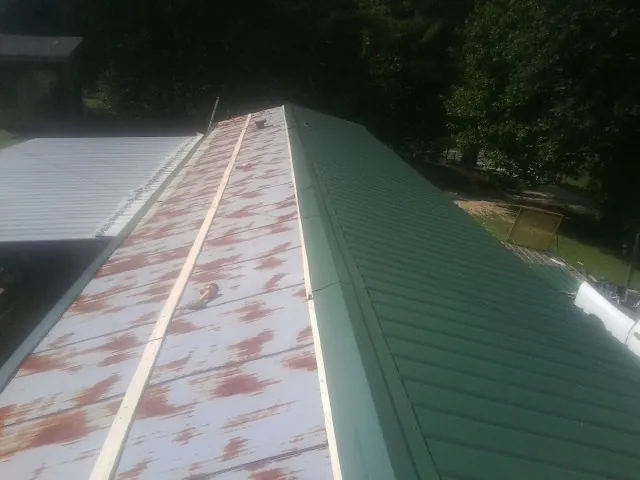 Old rusted panels beside newly installed green metal roofing — Wind Damage Roof Repair by Roofing Brothers in Vintondale