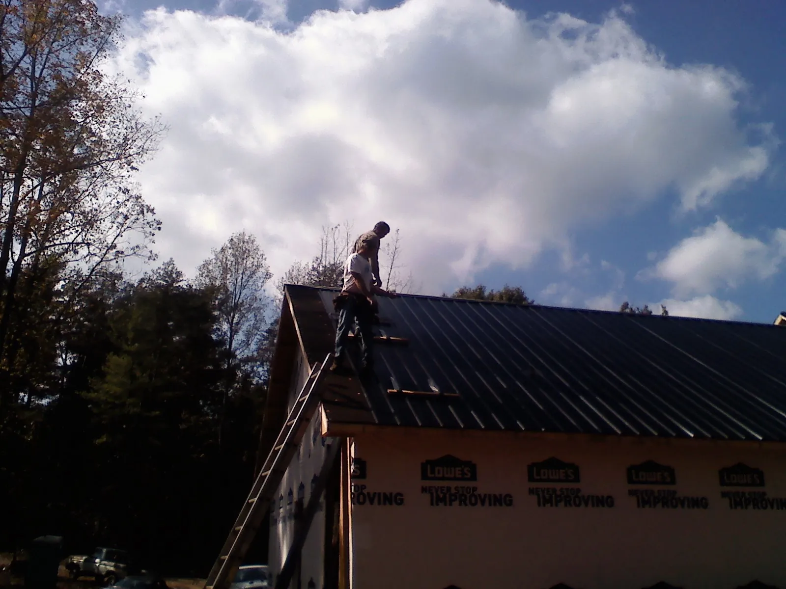 Roofer fastening dark metal panels high against a cloudy sky, from a Roof Inspection job in Vintondale