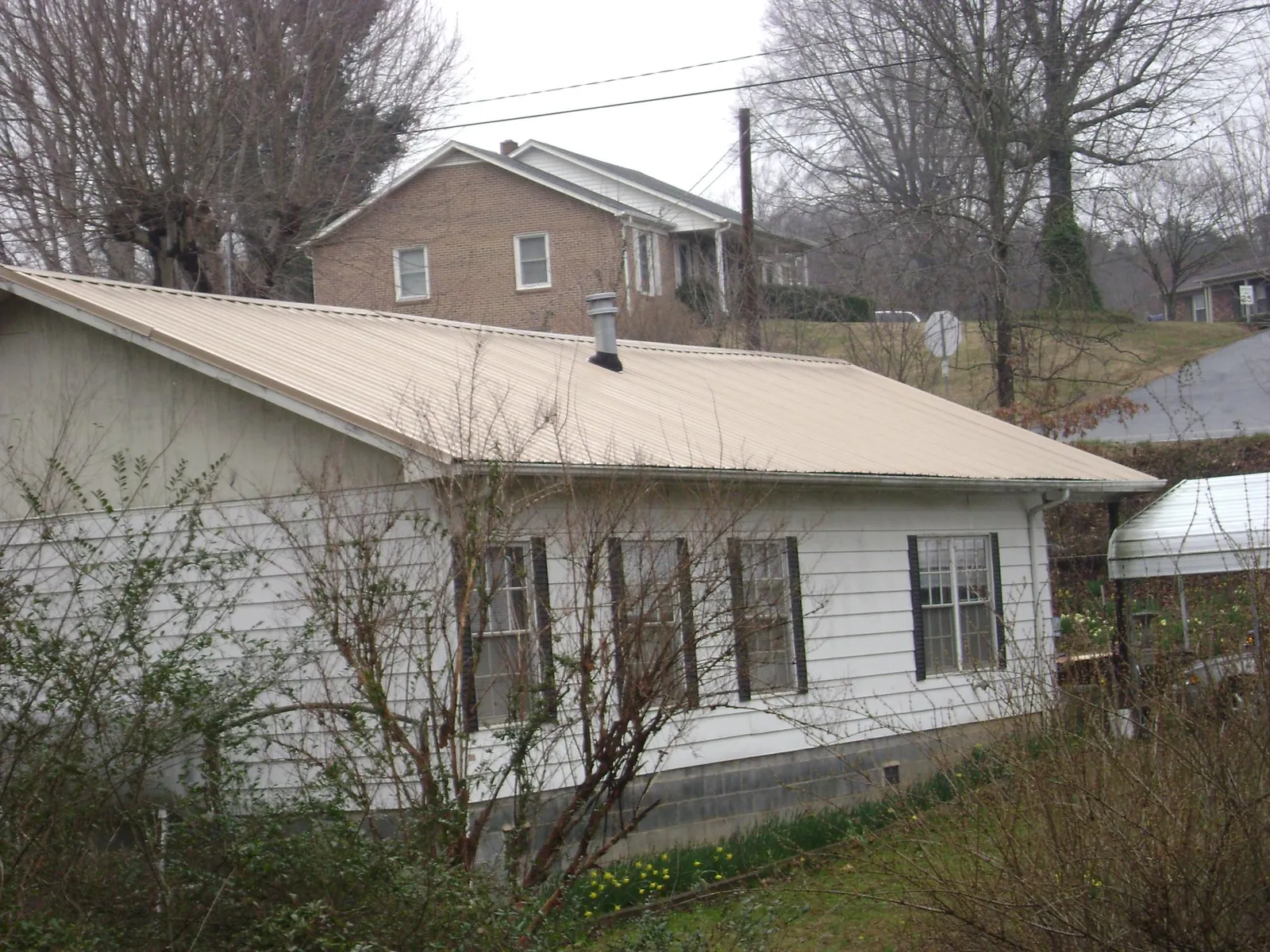 Tan metal roof on a white sided house set into a hillside — Commercial Roofing by Roofing Brothers in Vintondale