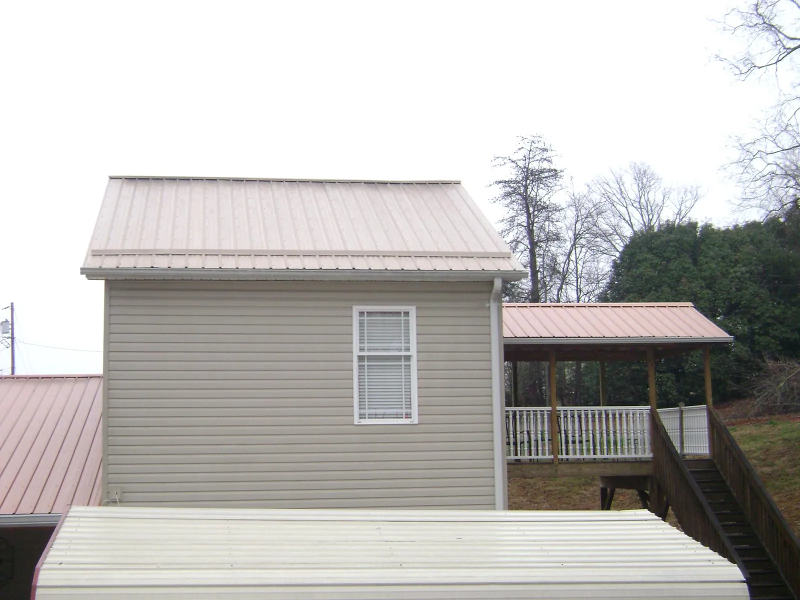 Tan metal roofs on a two story addition and attached porch, from a Roof Replacement job in Vintondale